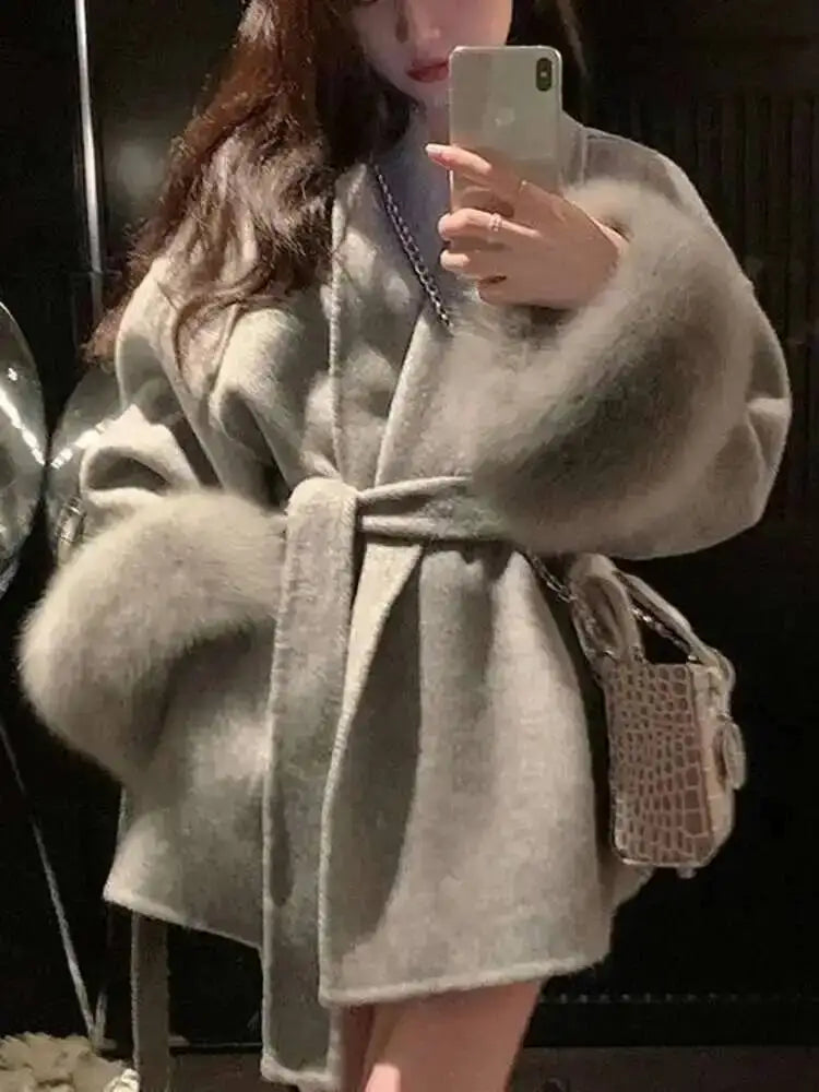 Kvinde iført grå pelsjakke med bælte, tager selfie med smartphone. Elegant vintermode, luksuriøs pels, trendy tilbehør.