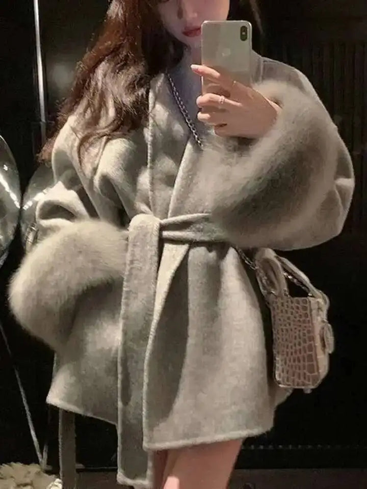 Kvinde iført grå pelsjakke med bælte, tager selfie med smartphone. Elegant vintermode, luksuriøs pels, trendy tilbehør.