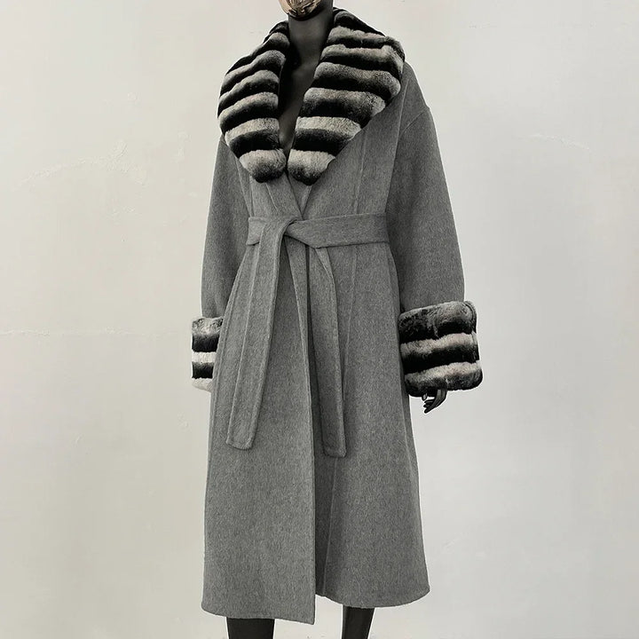 Grå frakke med bælte og sort-hvid stribet pelskrave og manchetter. Elegant vintermode, luksuriøs dameovertøj, stilfuldt design.