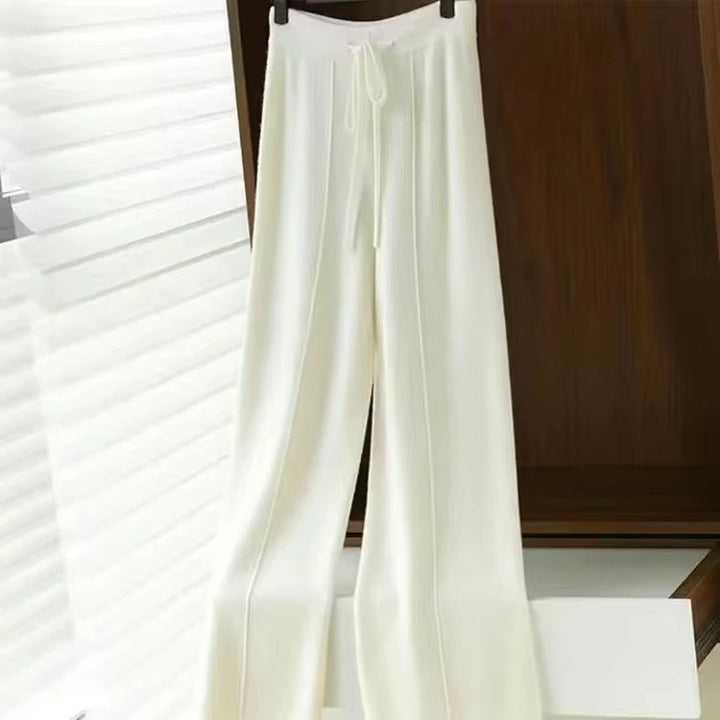 Hvide, løstsiddende bukser med snøre i taljen hænger på en bøjle. Moderne og stilfuldt design, perfekt til casual eller formel brug.