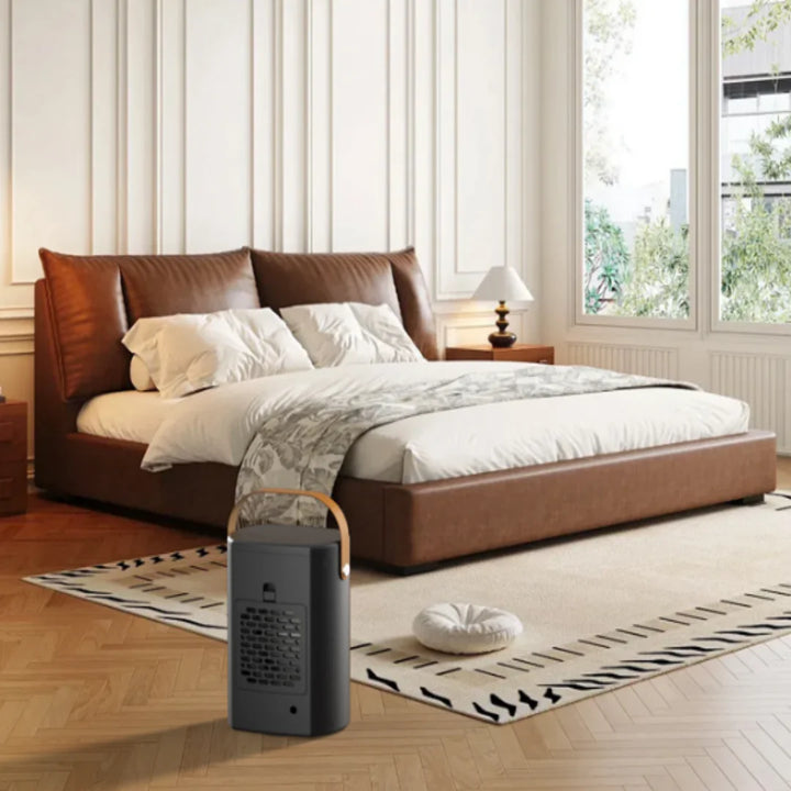 Lille sort varmeblæser med træhåndtag i moderne soveværelse med læderseng og tæppe. Effektiv opvarmning, stilfuldt design, kompakt størrelse.