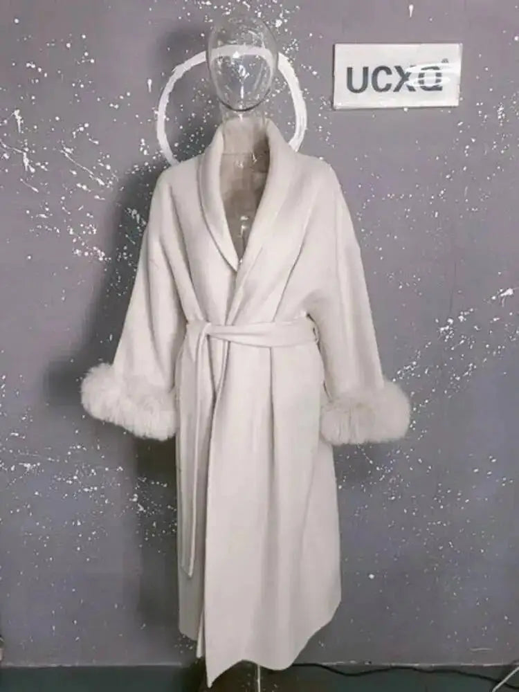 Hvid badekåbe med pelsmanchetter på gennemsigtig mannequin mod grå baggrund. Luksuriøs morgenkåbe, elegant design, vintermode.