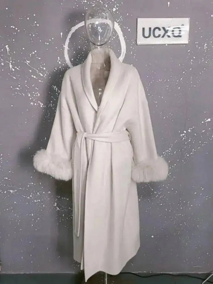 Hvid badekåbe med pelsmanchetter på gennemsigtig mannequin mod grå baggrund. Luksuriøs morgenkåbe, elegant design, vintermode.