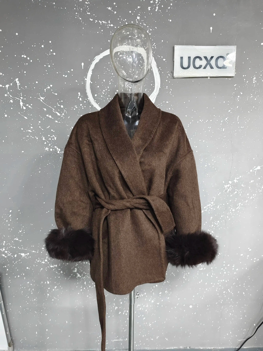 Brun uldfrakke med bælte og pelsmanchetter på mannequin. Moderne design, vintermode, stilfuld overtøj til kvinder.