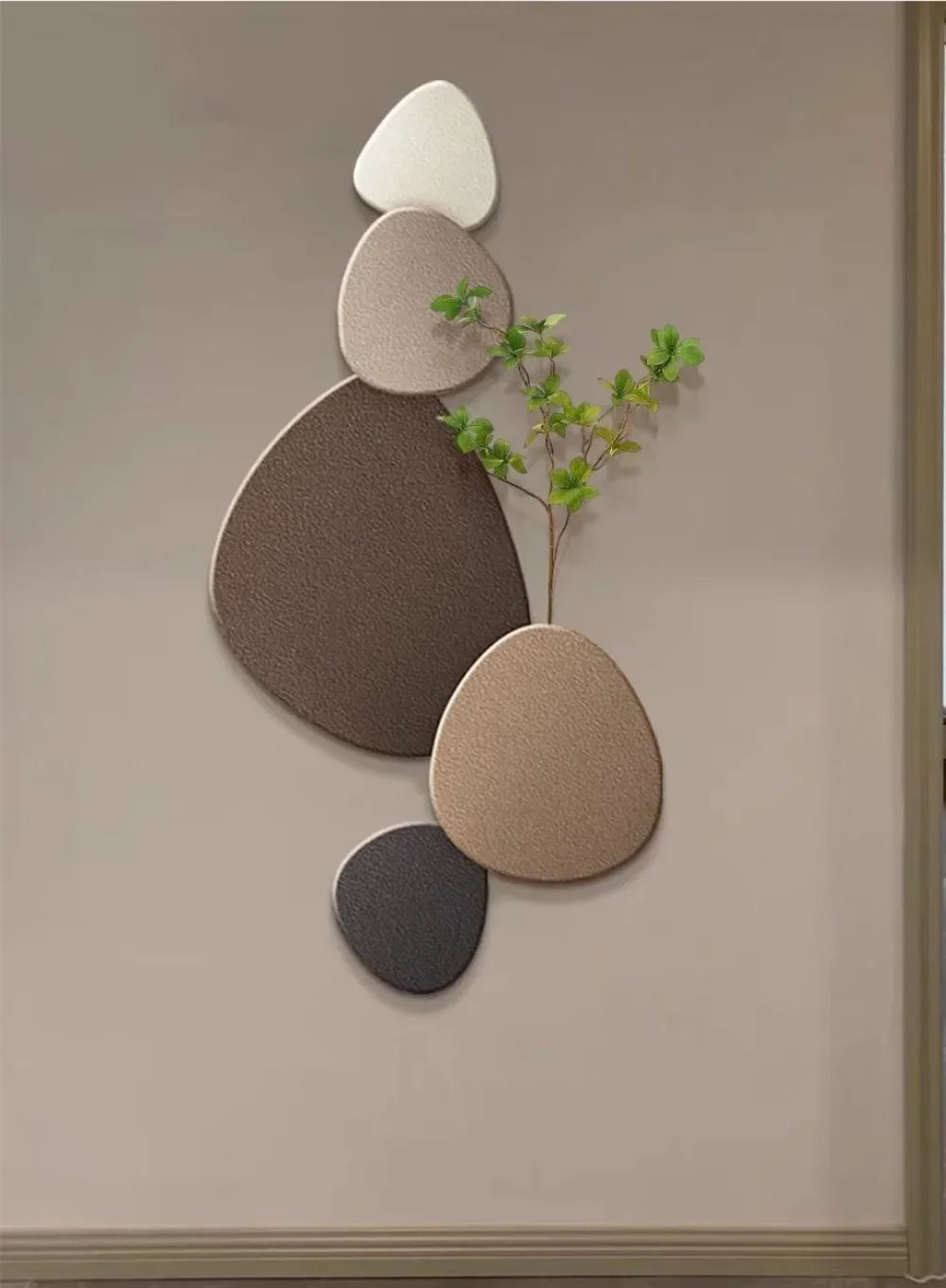 Dekorativ vægkunst med stenformede paneler i neutrale farver og en grøn plantegren. Moderne indretning, minimalistisk design, vægdekoration.