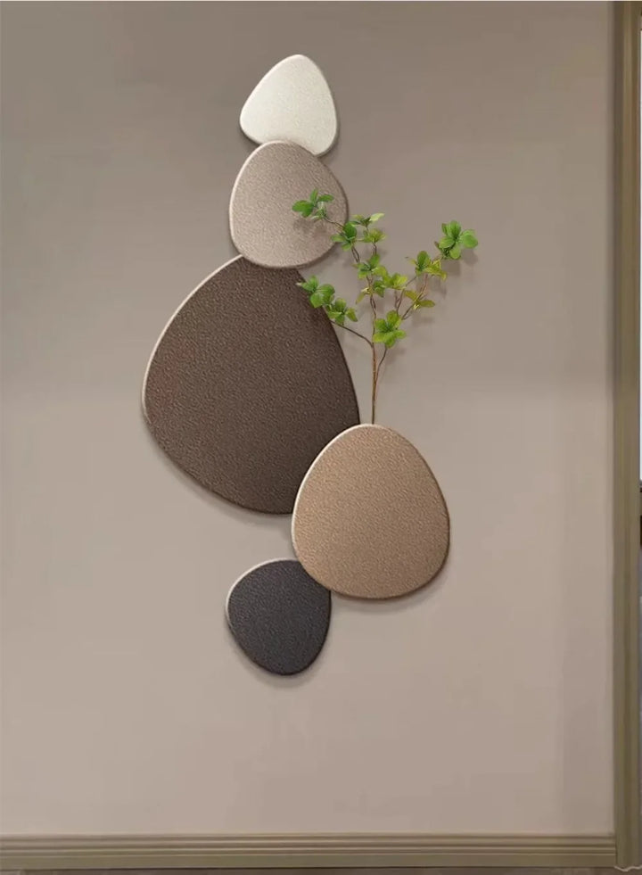Dekorativ vægkunst med stenformede paneler i neutrale farver og en grøn plantegren. Moderne indretning, minimalistisk design, vægdekoration.