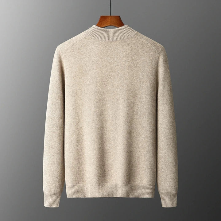 Beige uldtrøje på bøjle mod grå baggrund. Klassisk design, rund hals, lange ærmer. Perfekt til efterår og vinter. Stilfuld og varm beklædning.