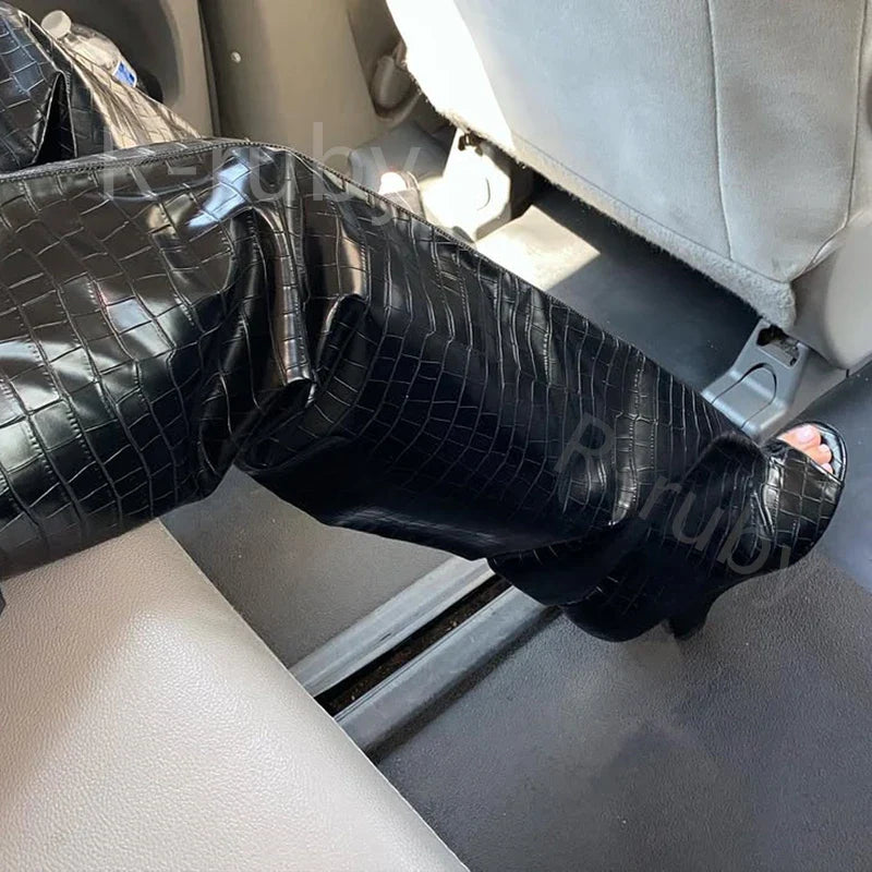 Sort krokodillemønstret læderbukser i bilsæde, moderne mode, stilfuldt design, luksuriøst look, trendy tøj, skinnende tekstur, kvindelig elegance.