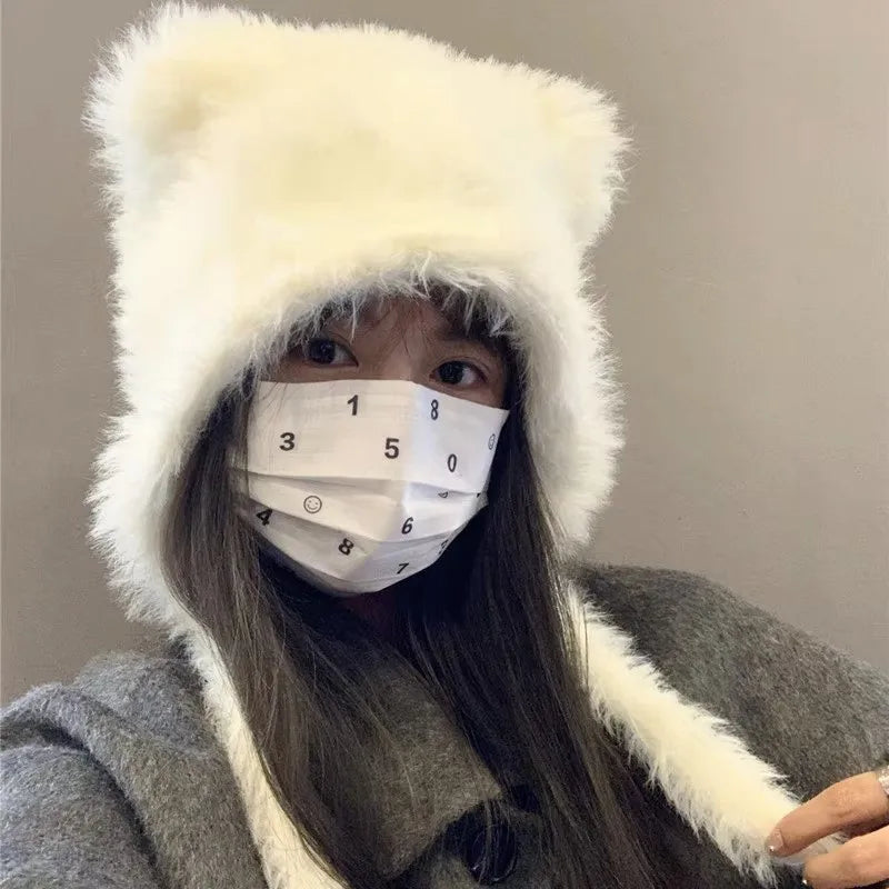 Ung kvinde iført hvid, fluffy bjørnehue og grå frakke, bærer en hvid maske med tal. Vintermode, trendy tilbehør, stilfuldt look.