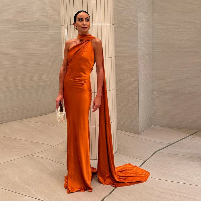 Kvinde i elegant, orange aftenkjole med asymmetrisk design, står i moderne interiør. Perfekt til mode, stil og luksusbeklædning.