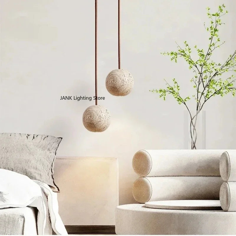 To pendellamper i beton hænger over en moderne stue med minimalistisk indretning. Ved siden af er en vase med grønne grene. Skandinavisk design.