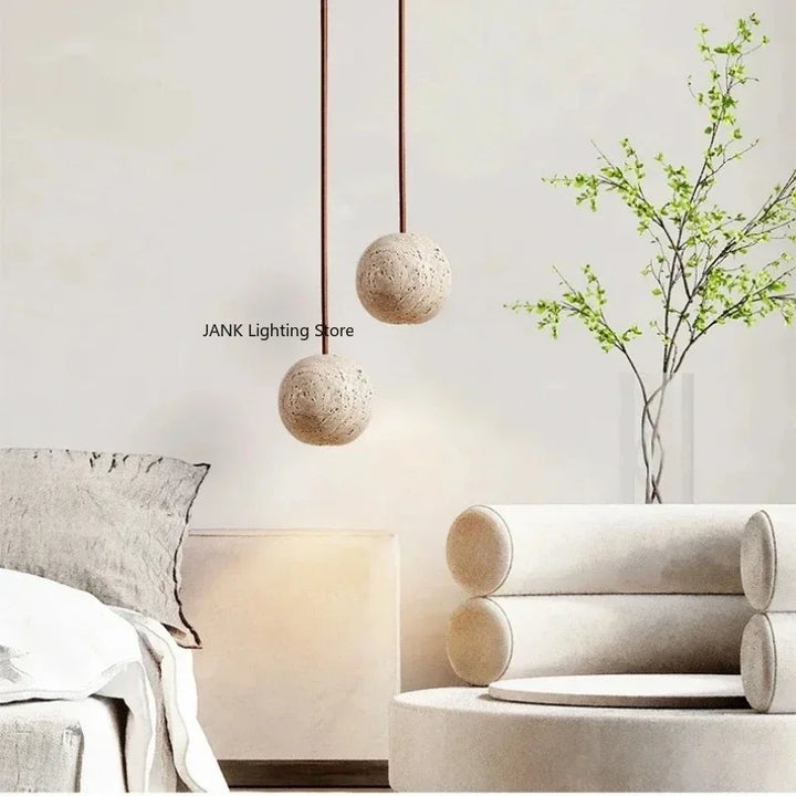 To pendellamper i beton hænger over en moderne stue med minimalistisk indretning. Ved siden af er en vase med grønne grene. Skandinavisk design.