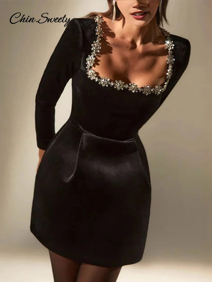 Kvinde i sort fløjlskjole med firkantet halsudskæring og blomsterdetaljer, elegant design, langærmet, perfekt til festlige lejligheder.