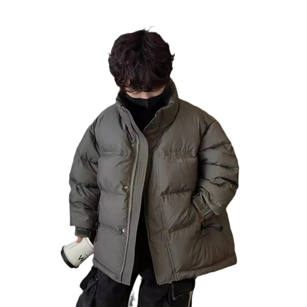 Dreng iført en stor, grå dunjakke med høj krave, sort trøje og sorte bukser. Vintermode, varm jakke, stilfuldt børnetøj.