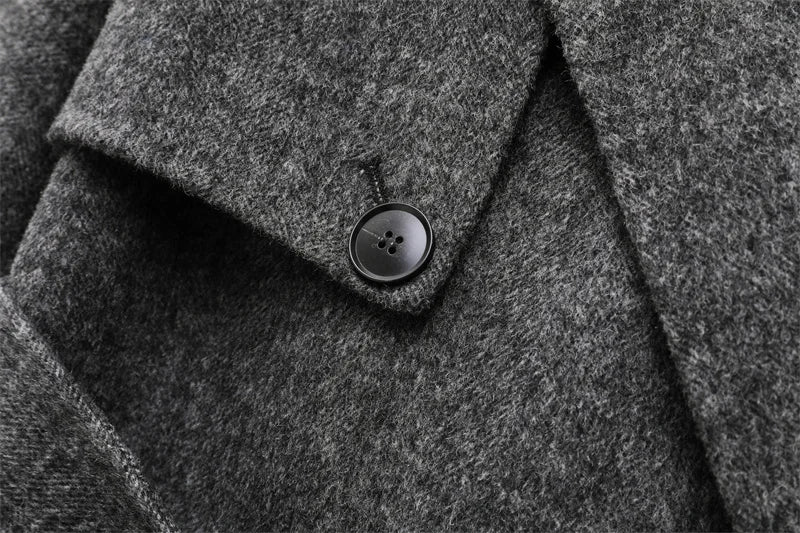 Grå uldfrakke med sort knap, tæt tekstur. Elegant vinterjakke, klassisk design, varm beklædning. Perfekt til stilfulde, kolde dage.