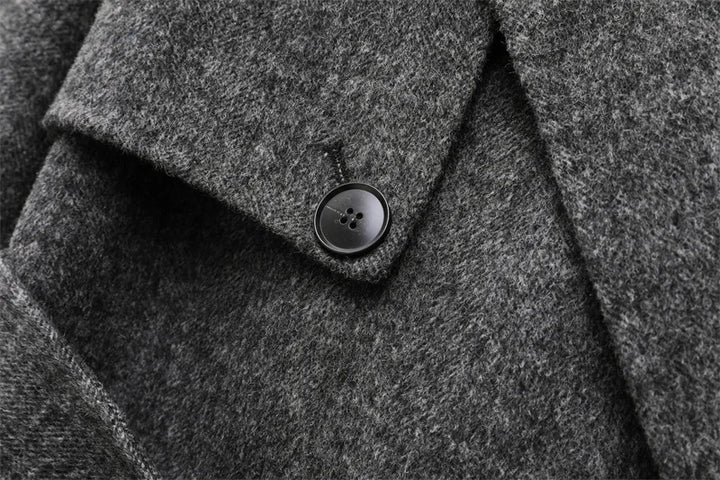 Grå uldfrakke med sort knap, tæt tekstur. Elegant vinterjakke, klassisk design, varm beklædning. Perfekt til stilfulde, kolde dage.