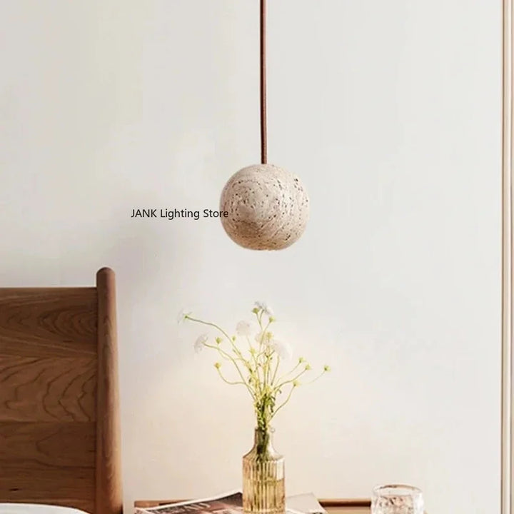 Hængelampe i natursten-look over natbord med vase og blomster, moderne skandinavisk indretning, minimalistisk belysning, stilfuldt soveværelse.