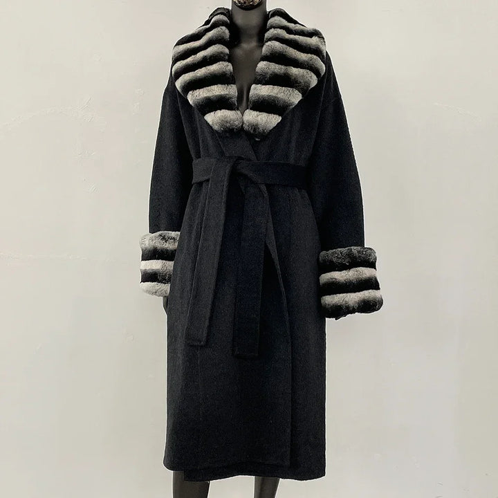 Sort frakke med bælte og stribede pelsdetaljer på krave og ærmer. Elegant vintermode, luksuriøs damefrakke, stilfuldt design.