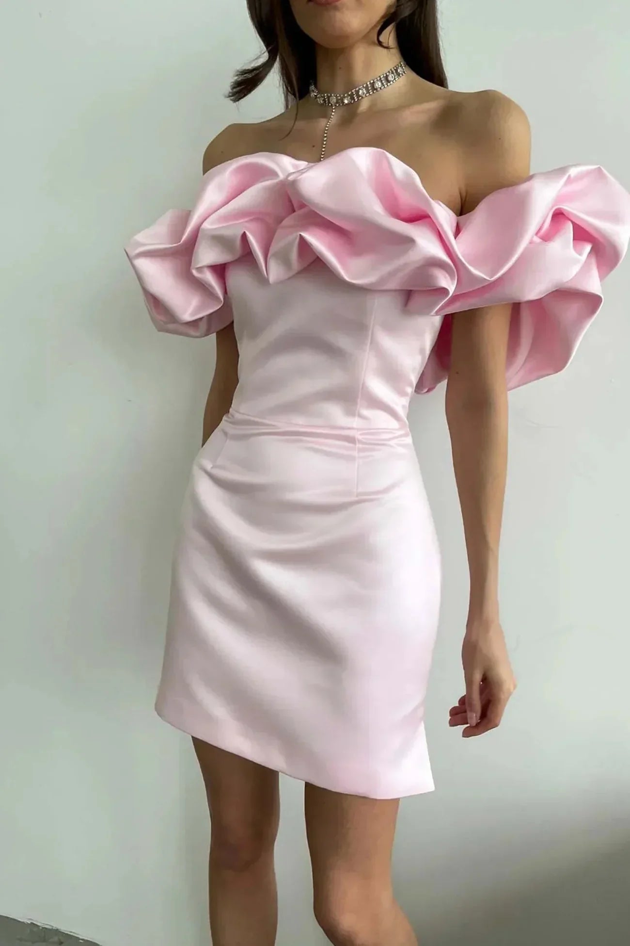 Kvinde i lyserød cocktailkjole med voluminøse off-shoulder flæser, elegant design, perfekt til festlige lejligheder.