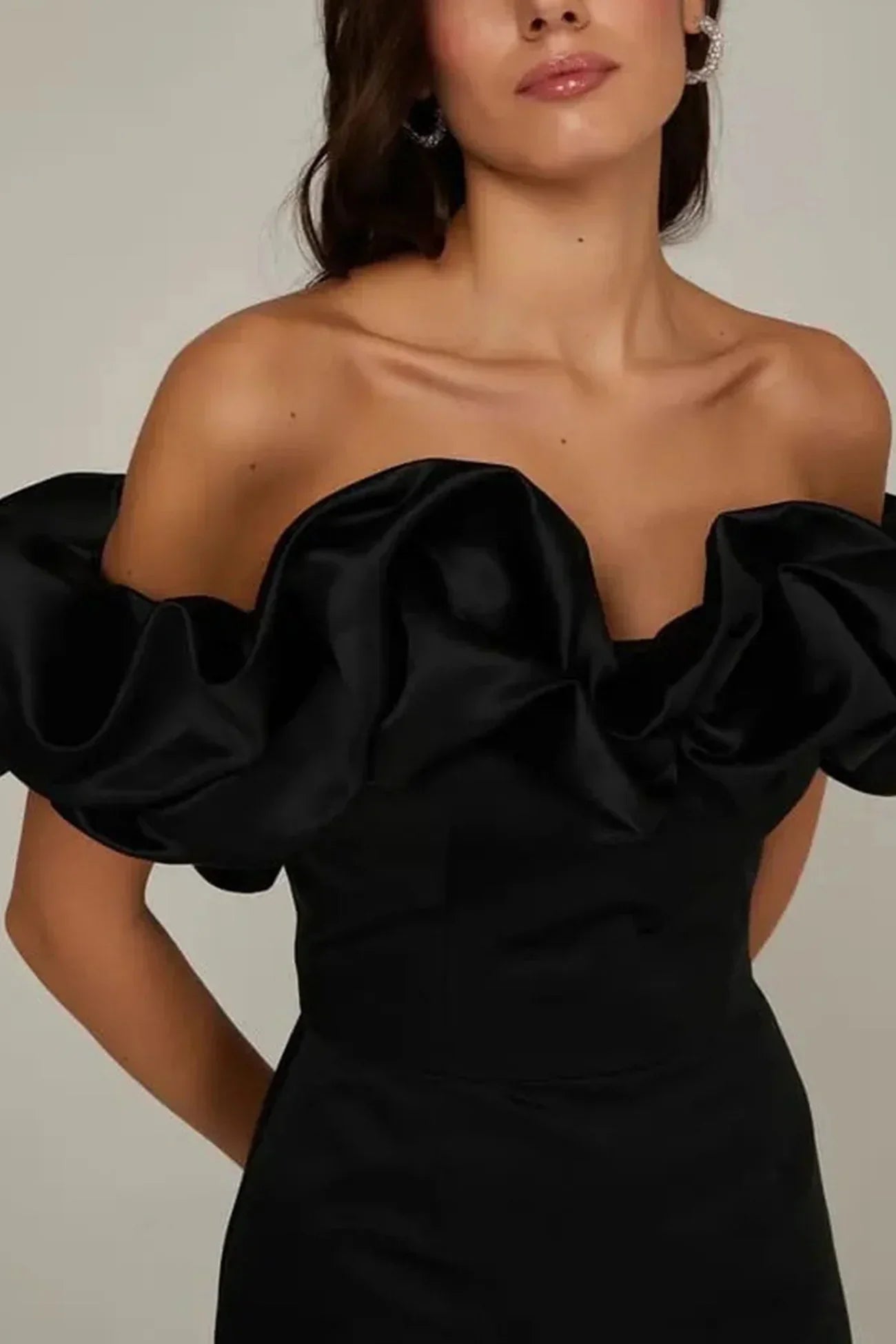 Kvinde i elegant sort off-shoulder kjole med voluminøse flæser. Perfekt til festlige lejligheder. Stilfuldt og moderne design.