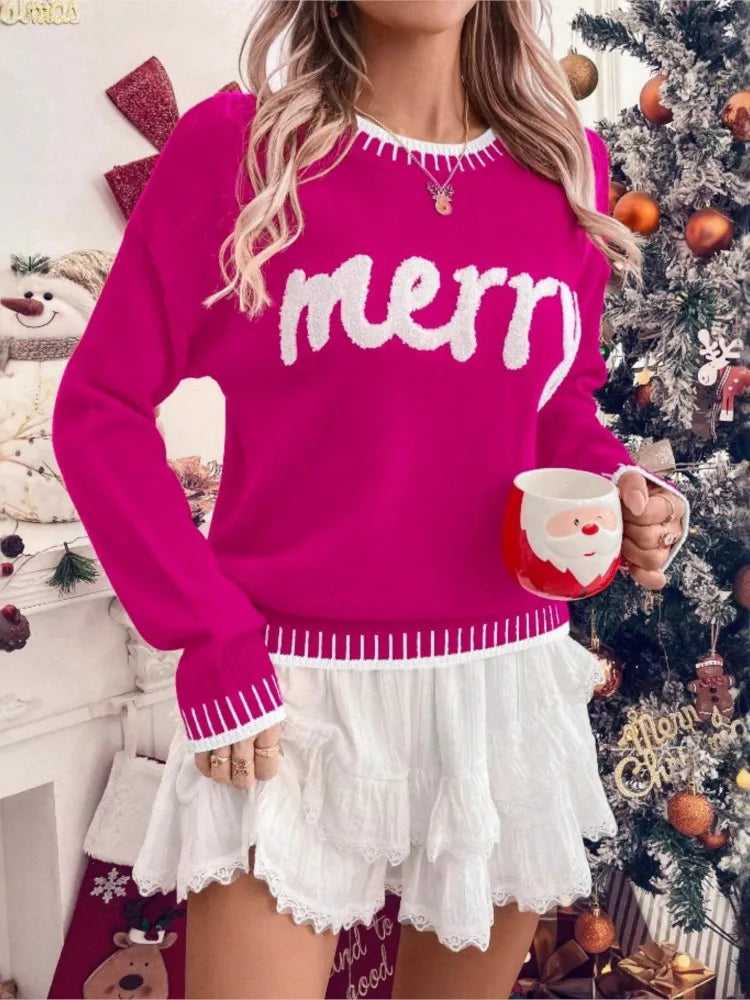 Kvinde i pink "merry" sweater og hvid nederdel, holder en rød julekop foran juletræ med pynt. Perfekt til julemode og festlig stil.