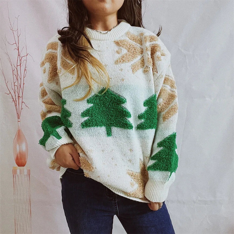 Kvinde iført hvid sweater med grønne juletræer og beige snefnug, poserer foran hvid baggrund. Perfekt til vintermode og juletema.
