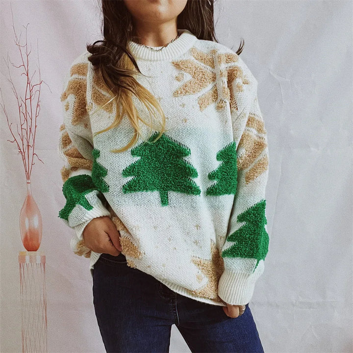 Kvinde iført hvid sweater med grønne juletræer og beige snefnug, poserer foran hvid baggrund. Perfekt til vintermode og juletema.