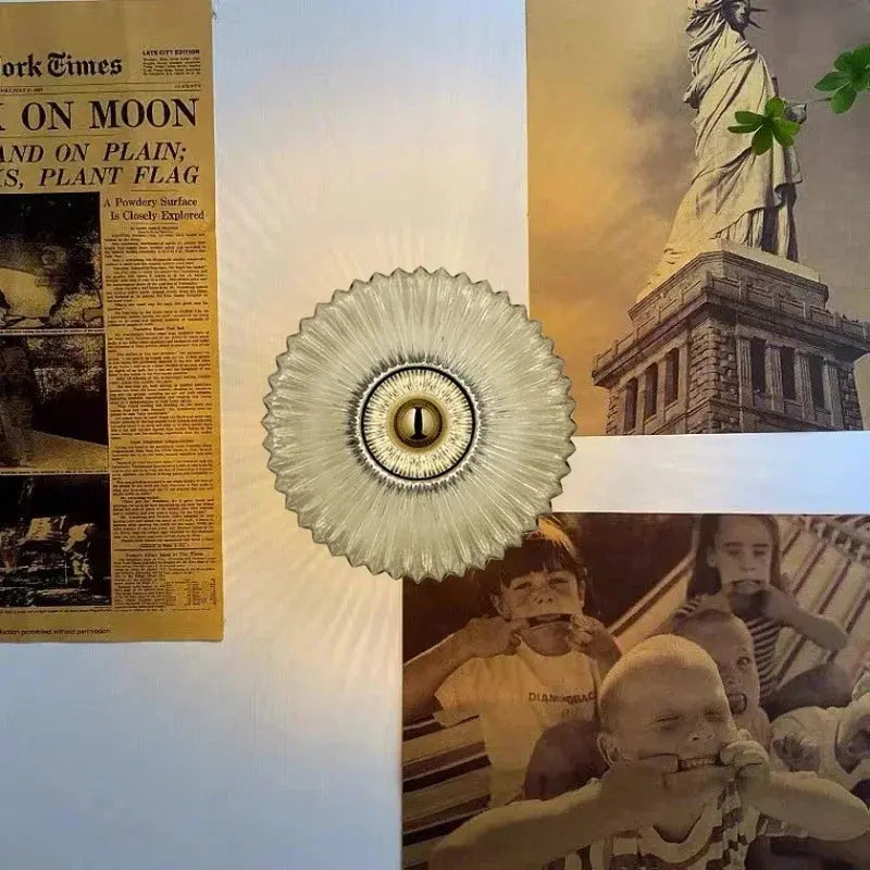 Vintage væglampe med glasdesign omgivet af historiske billeder, herunder Frihedsgudinden og en avisforside om månelandingen. Retro indretning.