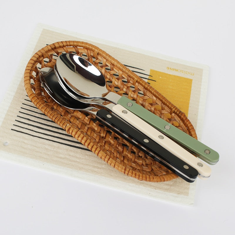 Flettet kurv med fire skeer i forskellige farver håndtag: grøn, sort, hvid og beige. Moderne bestik, køkkenudstyr, skandinavisk design.