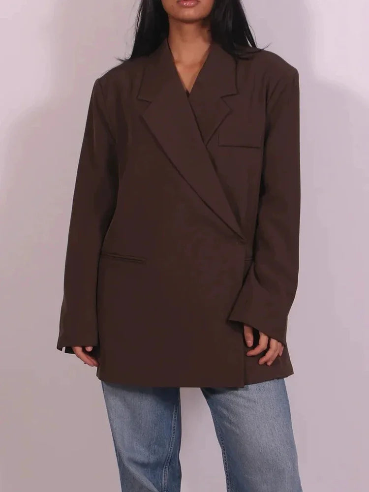 Kvinde iført brun oversized blazer og blå jeans. Trendy mode, minimalistisk stil, moderne tøjvalg, casual look, stilfuld damebeklædning.