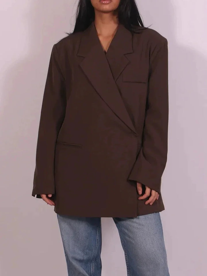 Kvinde iført brun oversized blazer og blå jeans. Trendy mode, minimalistisk stil, moderne tøjvalg, casual look, stilfuld damebeklædning.