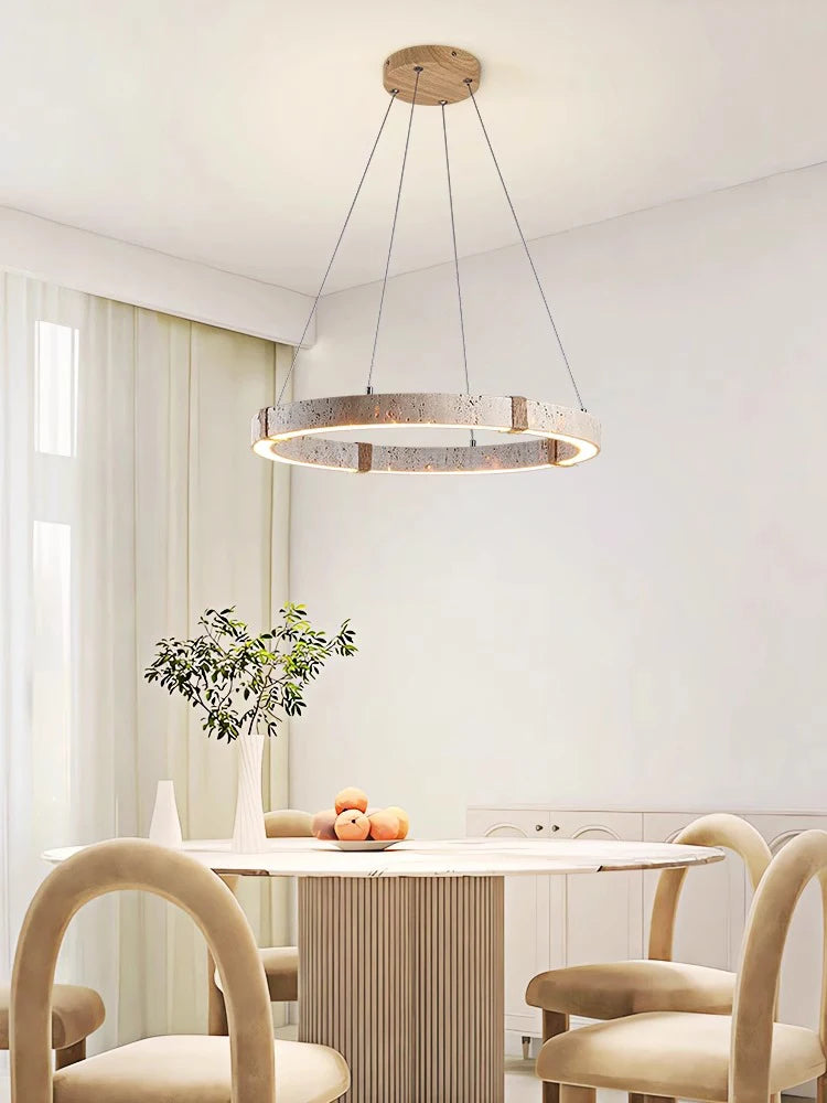 Moderne spisestue med rund træspisebord, beige stole og elegant cirkulær loftslampe. Minimalistisk indretning med friske appelsiner og grønne planter.