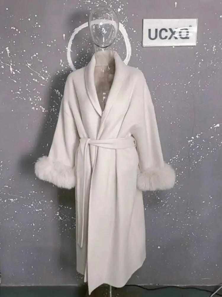 Hvid frakke med pelsmanchetter på gennemsigtig mannequin mod grå baggrund. Elegant vintermode, luksuriøs damefrakke, stilfuldt design.