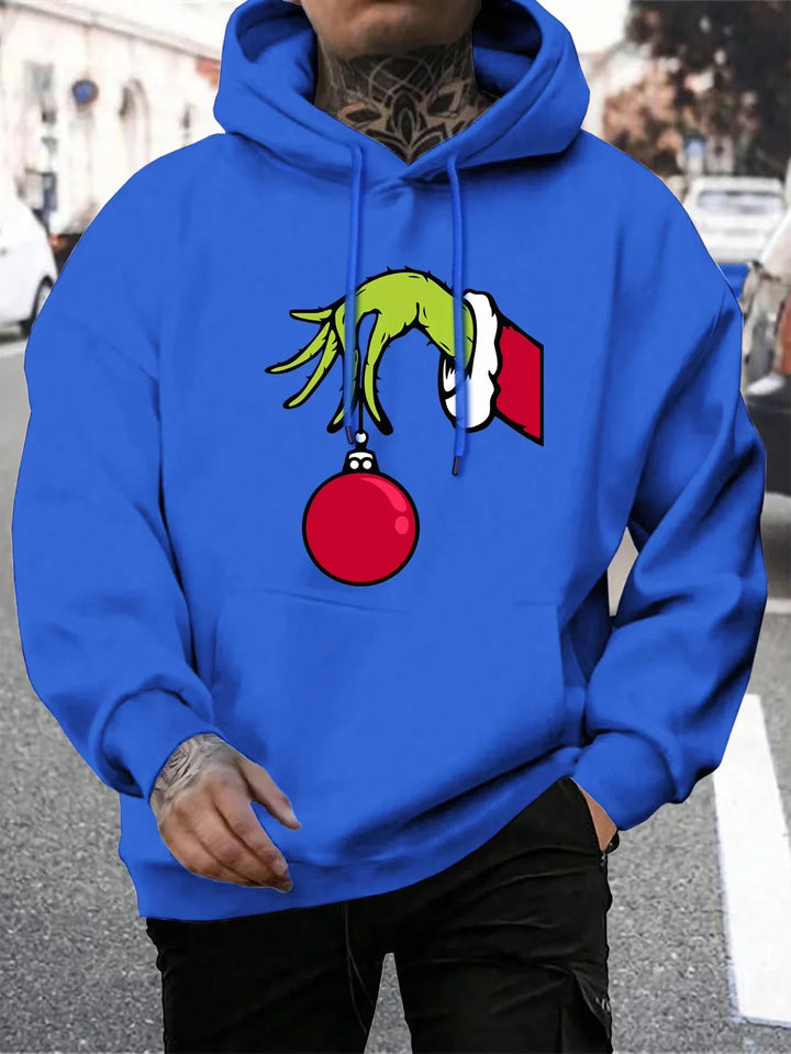 Mand iført blå hættetrøje med Grinch-motiv, der holder en rød julekugle. Perfekt til jul, streetwear, mode, unisex hoodie, vintertøj.