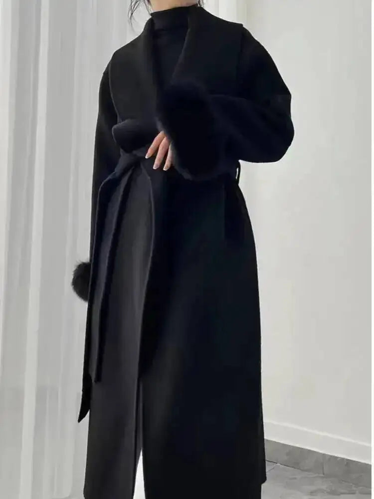 Sort uldfrakke med bælte, minimalistisk design, lange ærmer, kvinde i moderne tøjstil, elegant vintermode, stilfuld beklædning, skandinavisk look.
