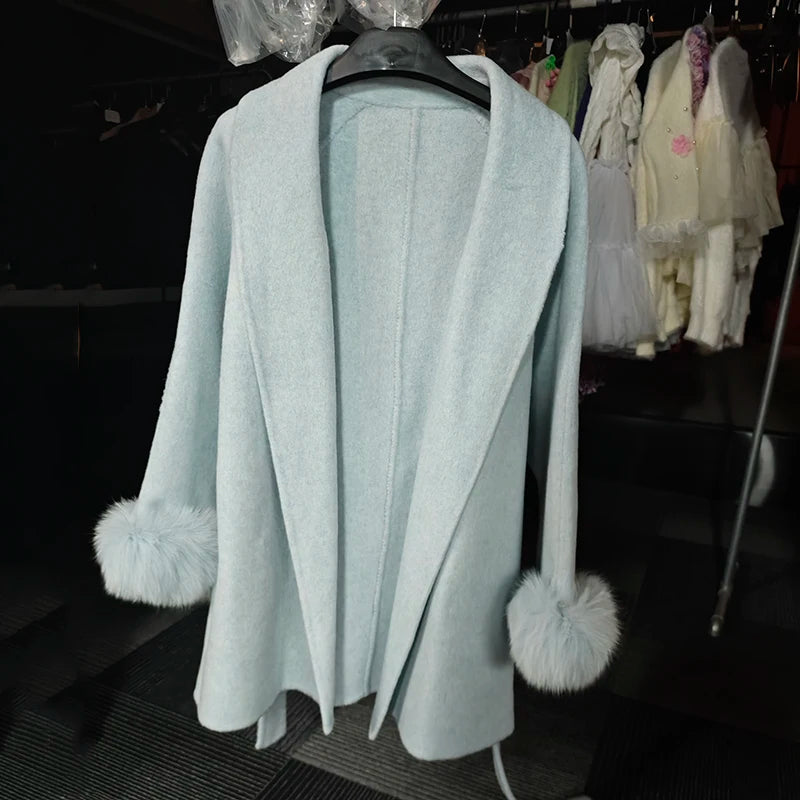 Lyseblå frakke med pelsmanchetter hænger på bøjle. Elegant design, perfekt til vintermode. Baggrund med tøj på stativ.