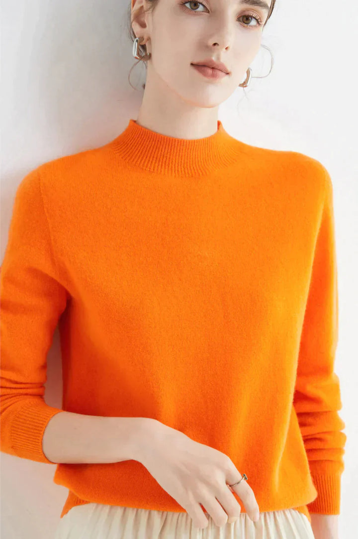 Kvinde iført en lys orange sweater, poserer mod en hvid baggrund. Moderne mode, minimalistisk stil, trendy efterårsbeklædning.
