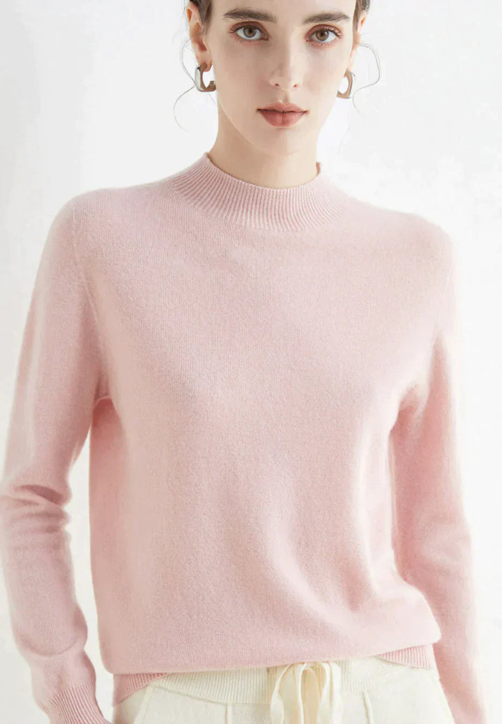 Kvinde iført lyserød cashmere sweater, stående mod hvid baggrund. Elegant og stilfuldt design, perfekt til modebevidste kvinder.