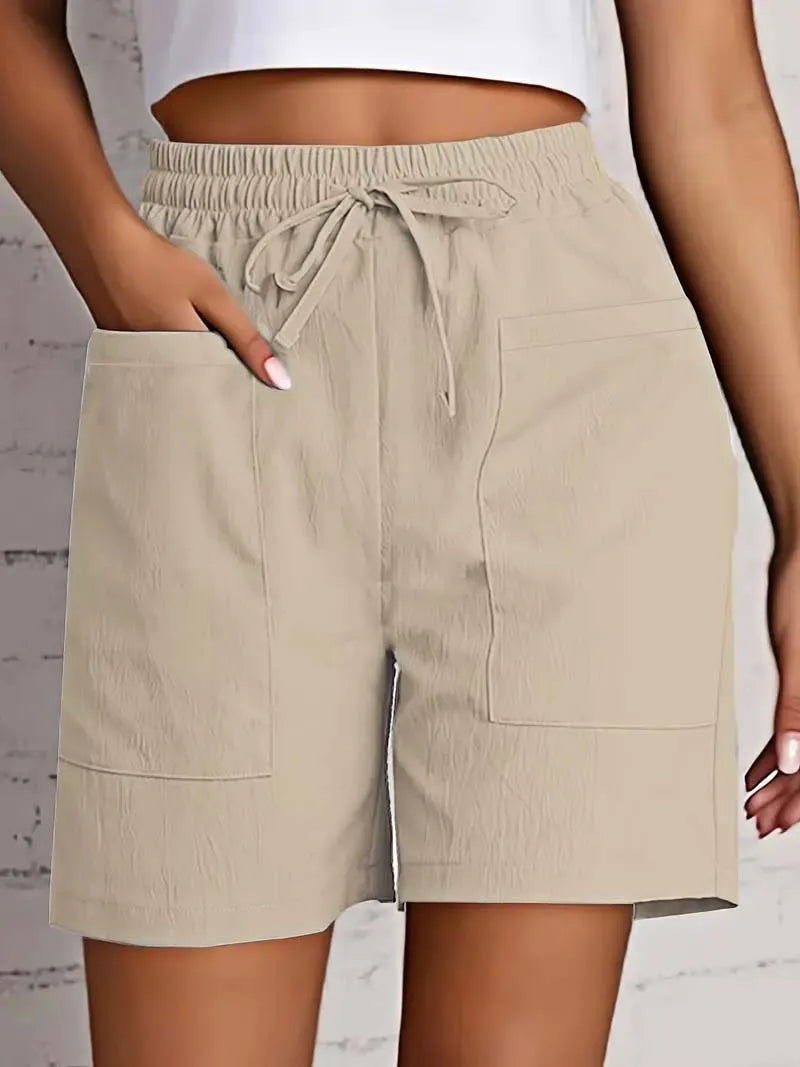 Beige shorts med elastisk talje og snøre, store forlommer, bæres af kvinde mod hvid baggrund. Komfortabelt sommertøj, casual stil.