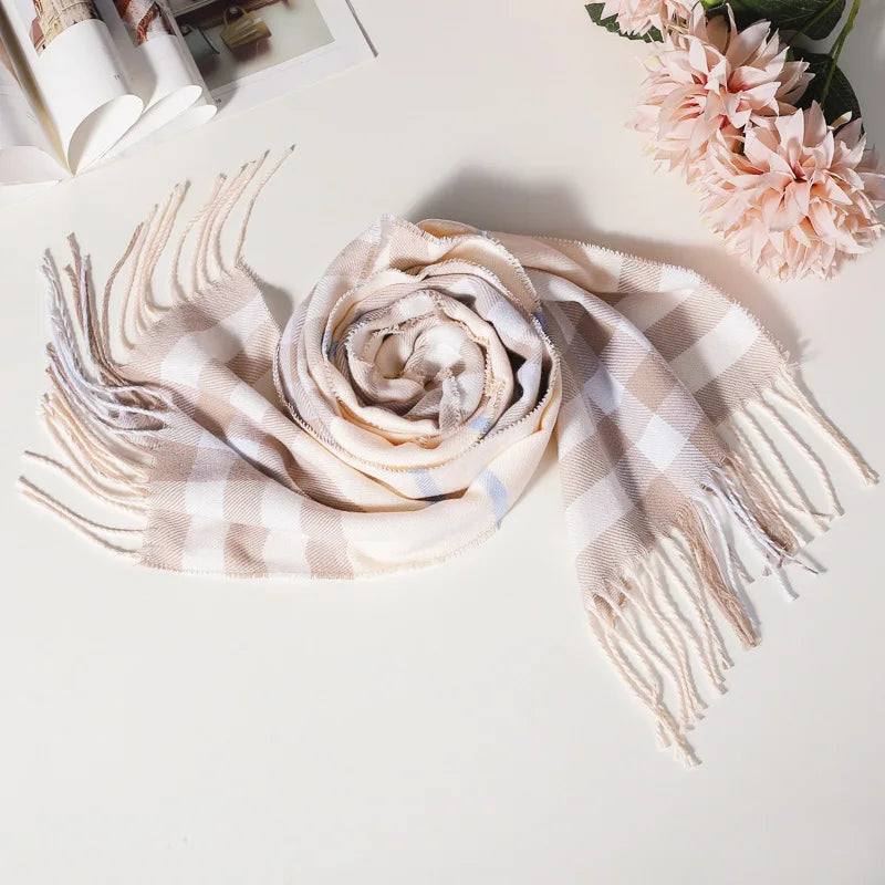 Beige og hvid ternet tørklæde med frynser, elegant design, ligger på bord ved siden af lyserøde blomster og åben bog. Perfekt til efterårsmode.