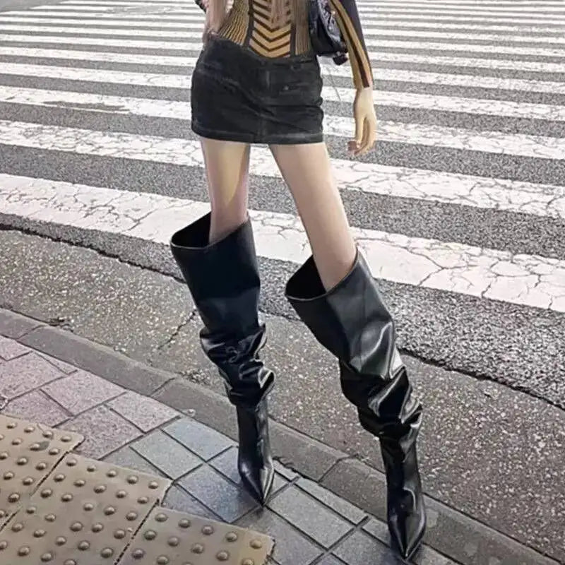 Kvinde iført sort miniskirt og overknee støvler på fortov ved fodgængerfelt. Mode, streetwear, stilfuldt outfit, byliv.