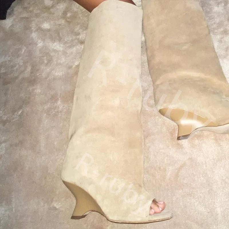 Beige knæhøje støvler med kilehæl og peep-toe design på tæppe. Moderne fodtøj, stilfulde støvler, trendy sko til kvinder.