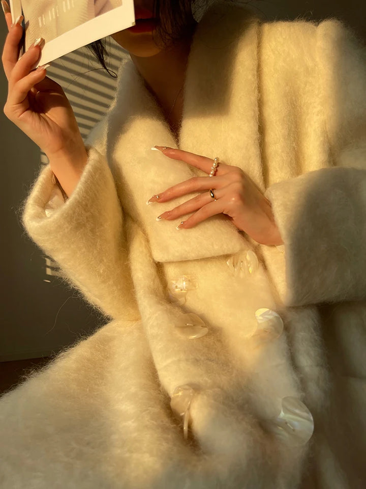 Kvinde iført elegant hvid pelsfrakke med store knapper, holder et kort op til ansigtet. Sollys skaber skygger, fremhæver tekstur og detaljer.