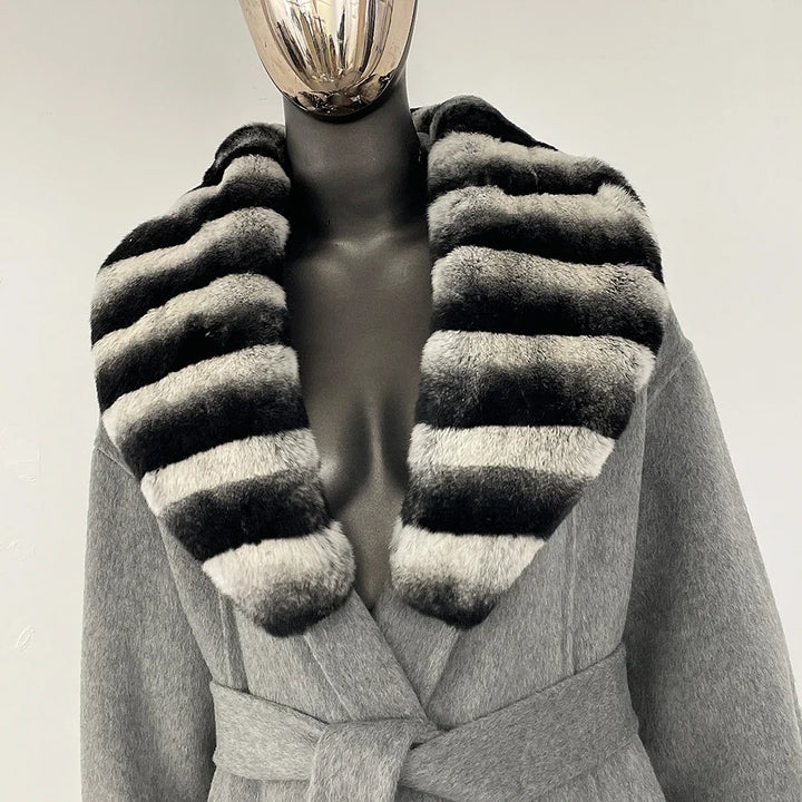 Grå frakke med sort og grå stribet pelskrave på mannequin. Elegant vintermode, luksuriøs damebeklædning, stilfuldt design.