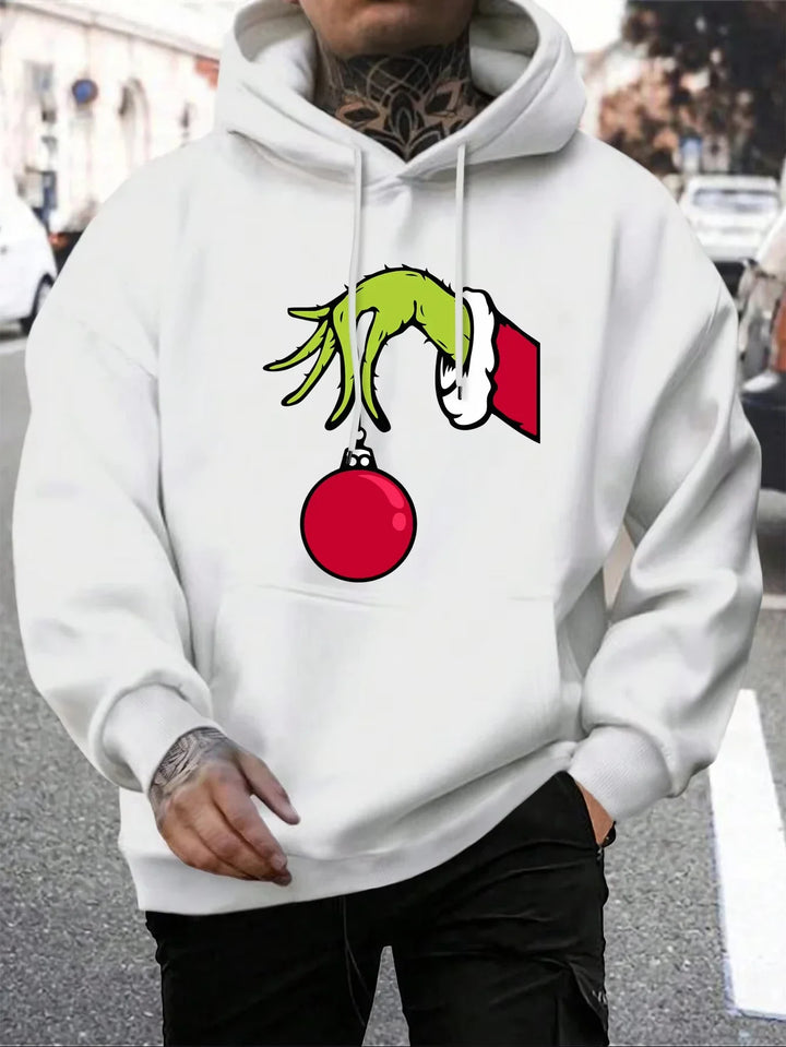Mand iført hvid hættetrøje med Grinch-motiv, der holder en rød julekugle. Perfekt til jul, streetwear, unikt design, vintermode.