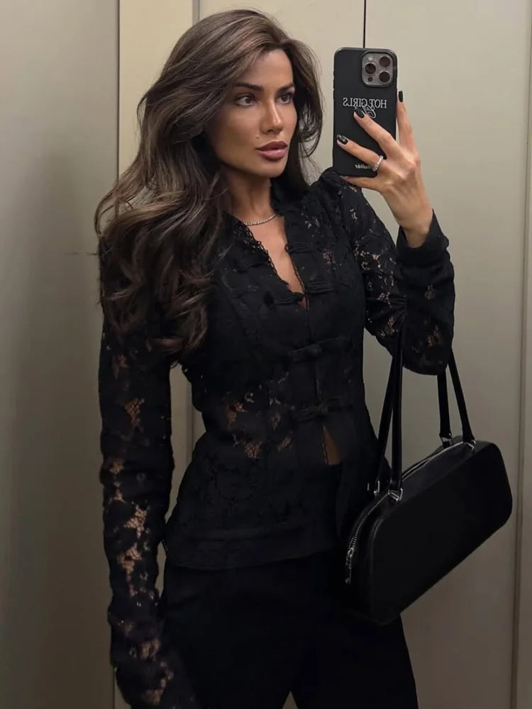 Kvinde i sort blondebluse tager selfie i spejl, holder sort taske. Langt, bølget hår. Moderne mode, stilfuldt outfit, selfie i elevator.