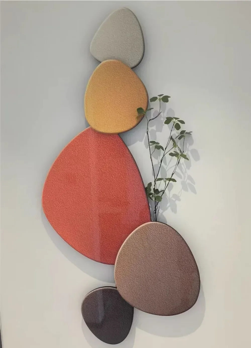 Dekorativ vægkunst med farverige, geometriske former og en lille plantegren. Moderne design, hjemmedekoration, kunstnerisk vægpynt.