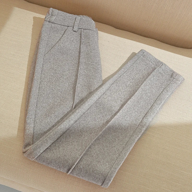 Grå uldbukser med sildebensmønster, foldet på beige sofa. Stilfulde herrebukser, klassisk design, perfekt til formelle lejligheder.