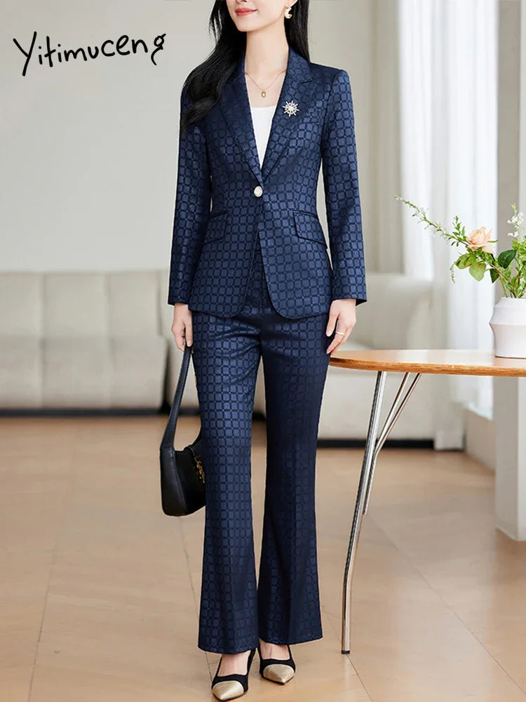 Kvinde i elegant mørkeblåt jakkesæt med mønster, bærer sort taske. Perfekt til forretningsmøder. Moderne kontorindretning i baggrunden.