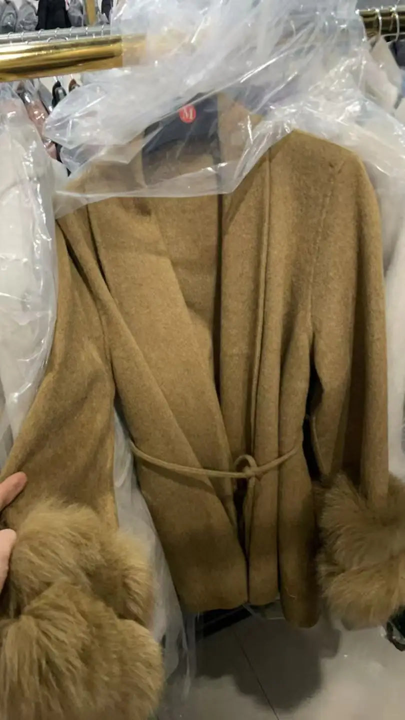 Brun uldfrakke med pelsmanchetter, hængende på bøjle. Elegant vinterjakke, moderne design, varm beklædning til kolde sæsoner.